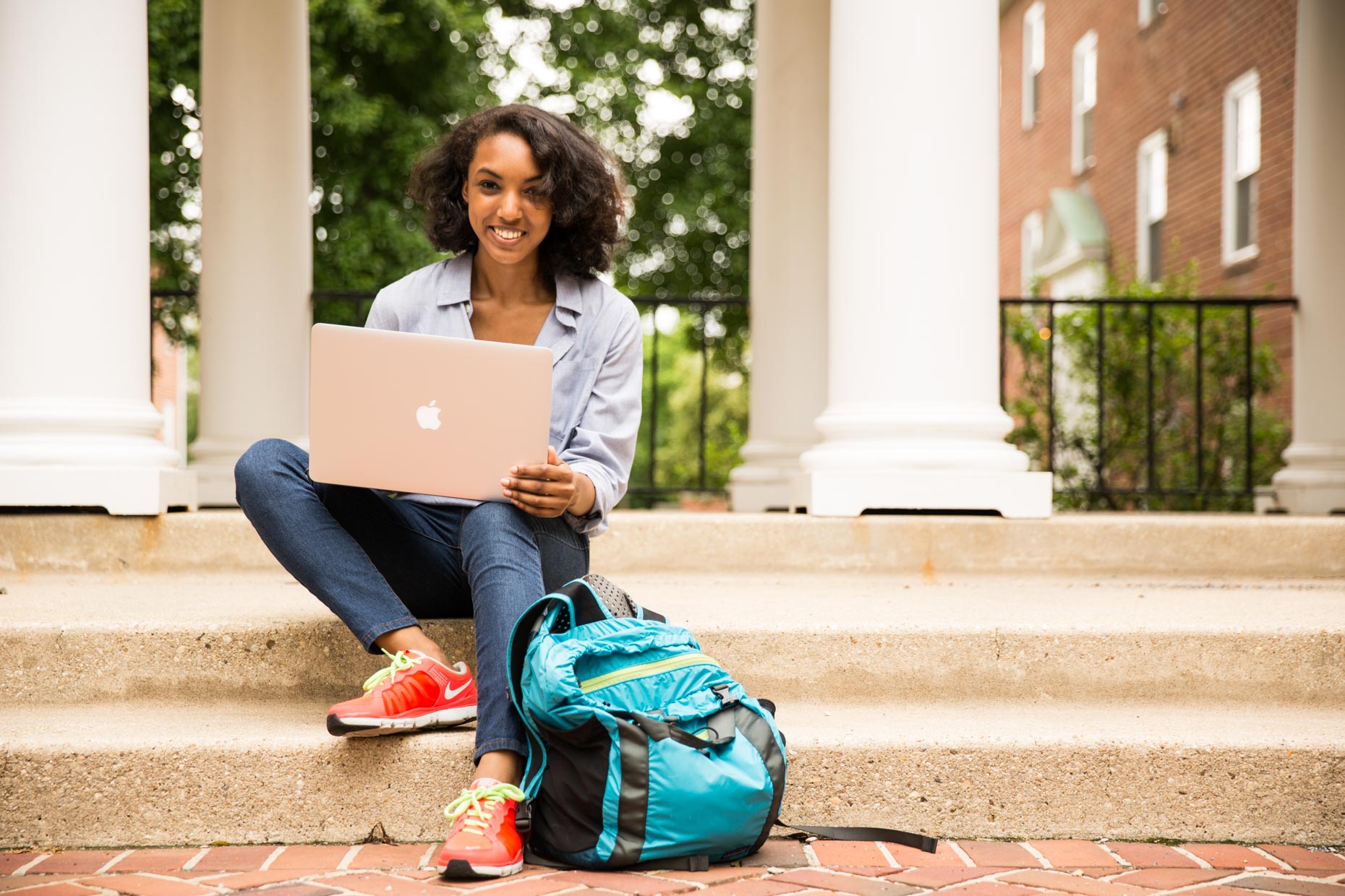Female African American  college student sitting on steps with laptop.