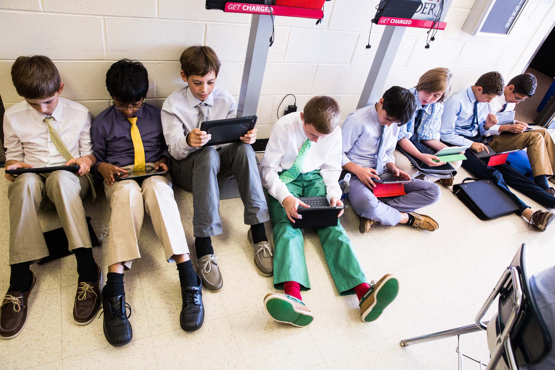 Students studying with laptops in school hallway.