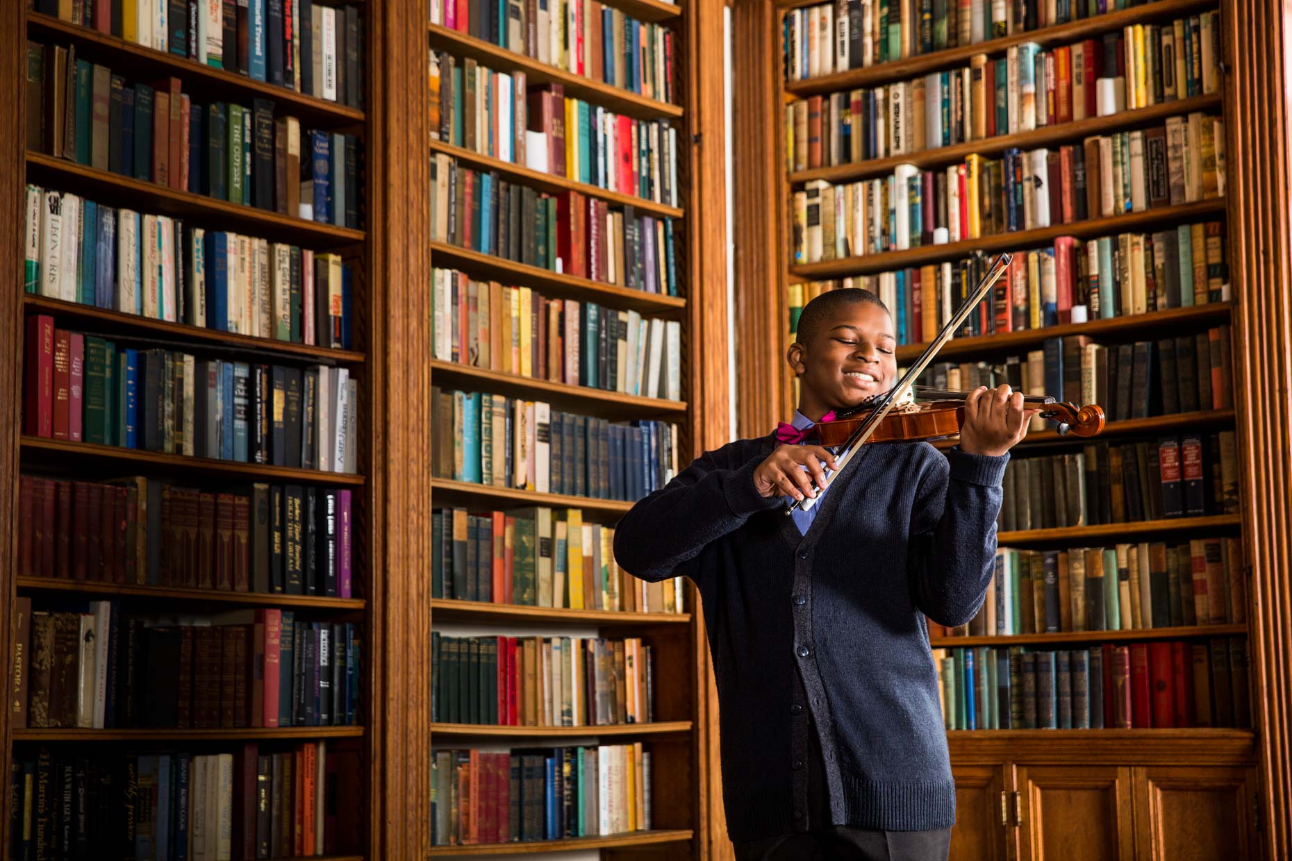 African American boy playing the violin in a library.