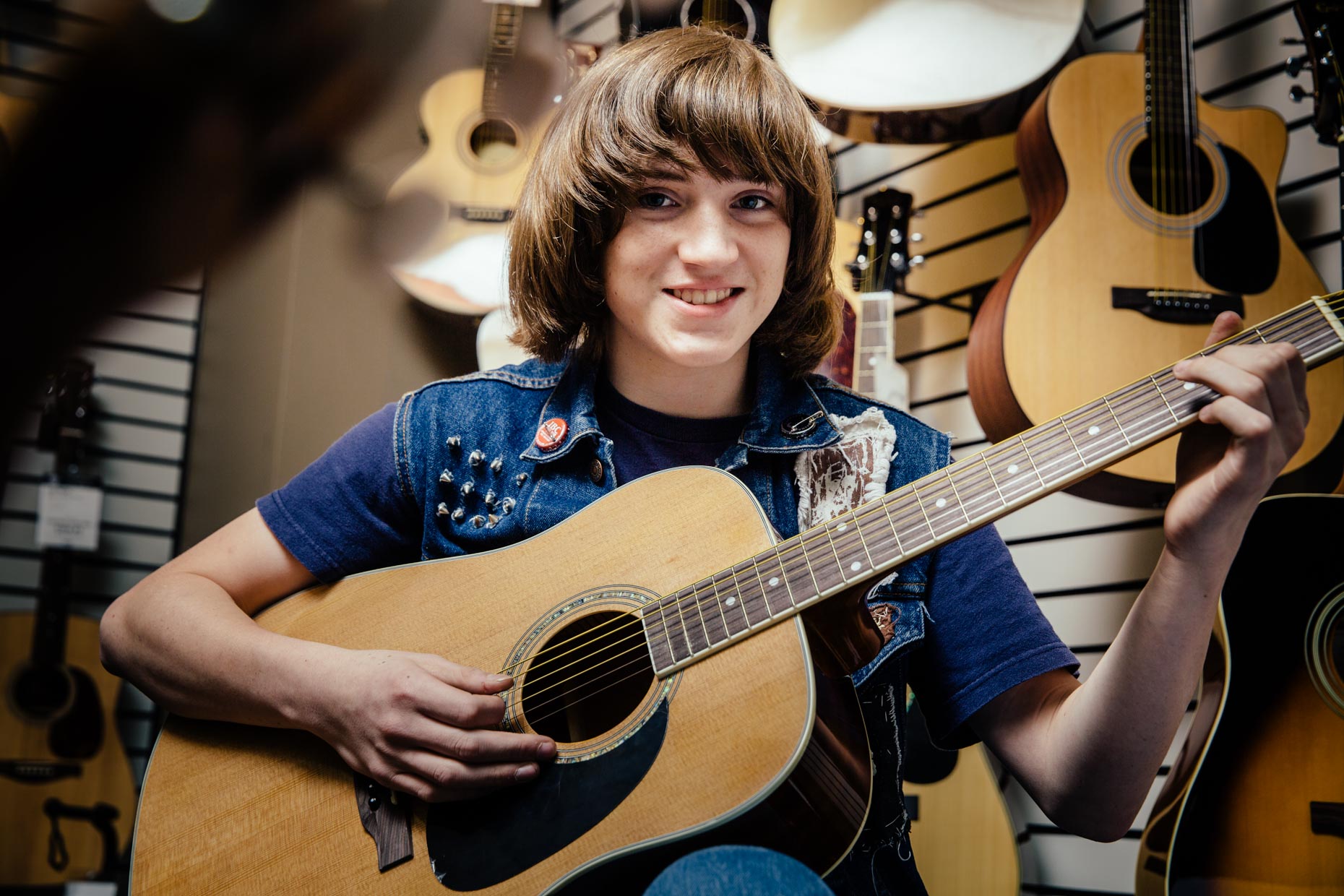 Boy with long hair and guitar in music store.