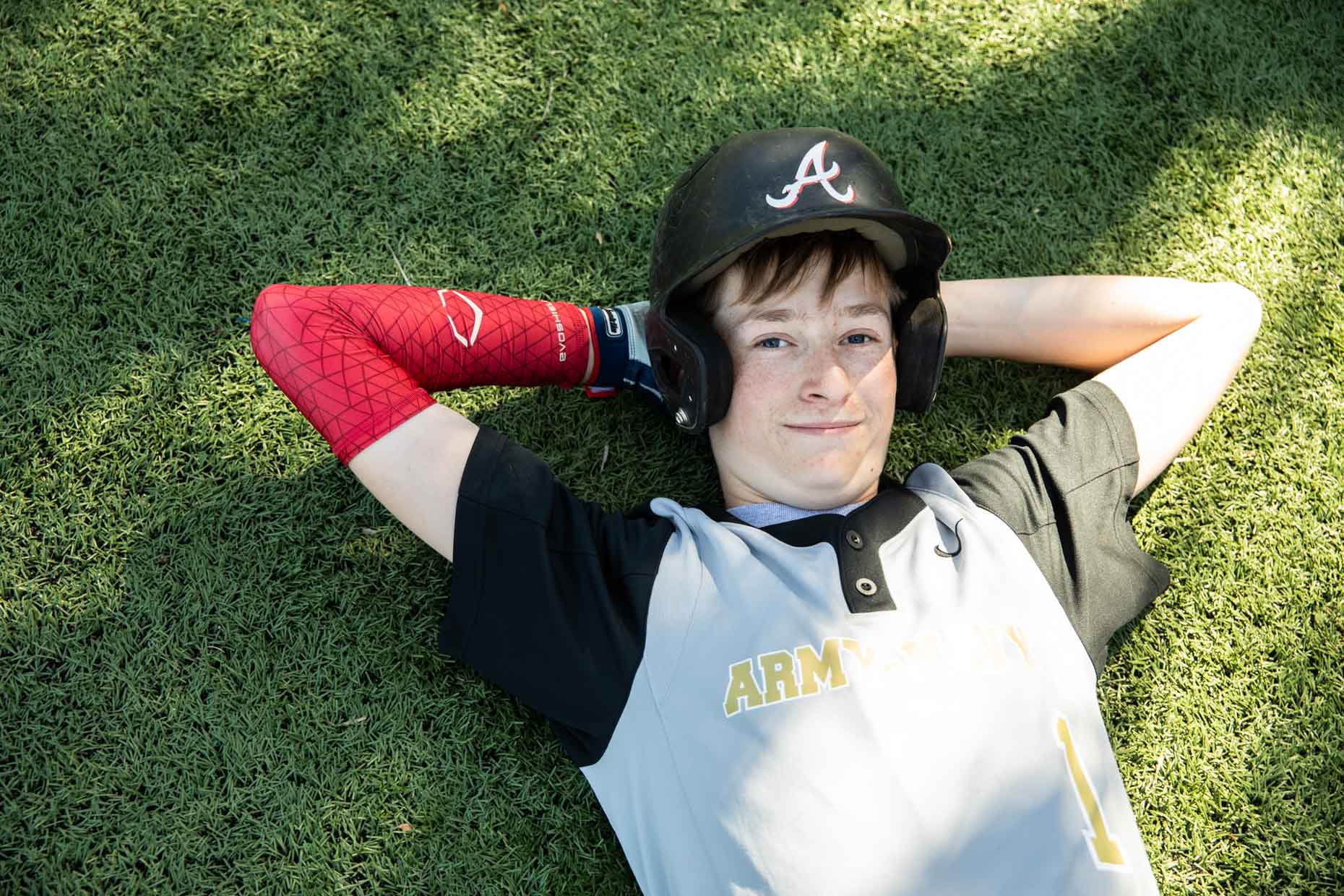 Young Baseball player laying on grass with batter helmet.
