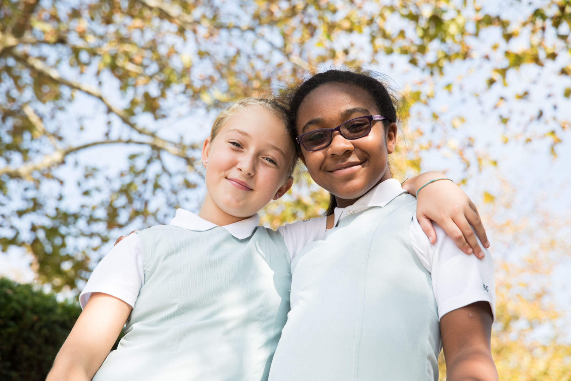 Two school girls smiling with arms around each other.