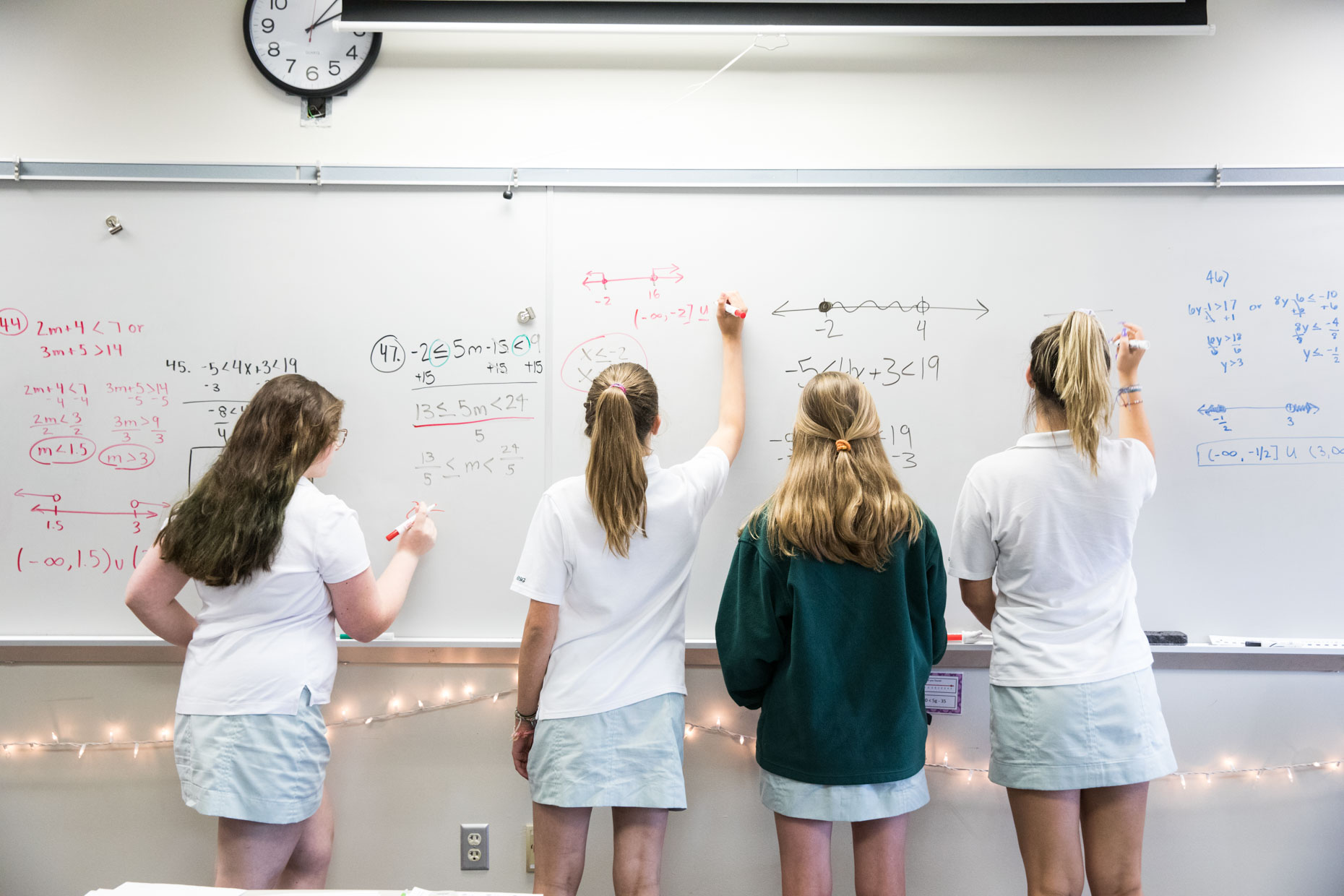 Girls in uniform writing on white board in classroom.